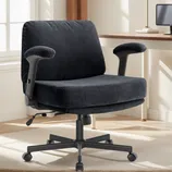 Black mesh office chair with cushioned armrests and adjustable height on a wheeled base in a home office setting with a desk, lamp, and computer.