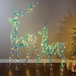 Two illuminated reindeer figures with LED lights are depicted, featuring a holographic design. A decorated Christmas tree and a wrapped gift box are nearby, creating a festive atmosphere.