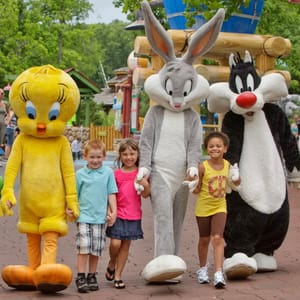 Children walk with costumed characters resembling Tweety, Bugs Bunny, and Sylvester in an amusement park setting.