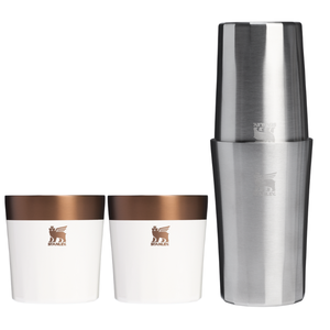 Stanley 3pc Cocktail Set includes a stainless steel cocktail shaker and two matching cups with a copper top and white bottom. The items feature the Stanley logo and are designed for mixing and serving drinks.