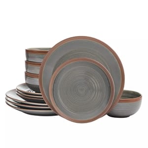 The Food Network Colby Dinnerware Set features plates and bowls with earthy tones and concentric circle designs. Each piece has a rustic charm with muted gray and brown hues.