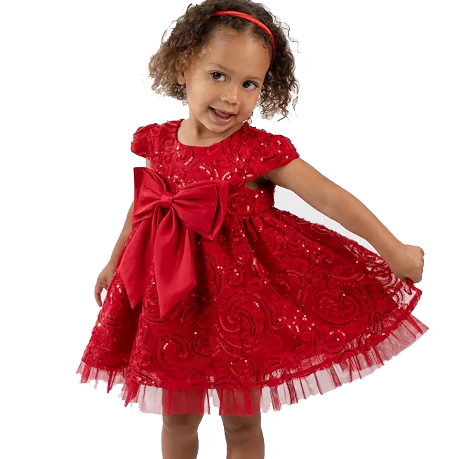 A toddler is wearing a bright red dress adorned with a large bow and lace detailing, paired with a matching headband.