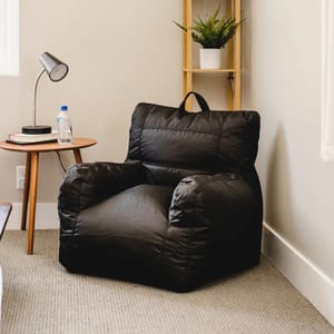 A black Big Joe chair with a soft, cushioned design and an integrated drink holder, situated in a cozy room corner next to a wooden side table and a bookshelf.
