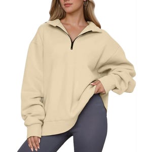 A woman is wearing an oversized beige quarter-zip pullover sweatshirt paired with gray leggings.