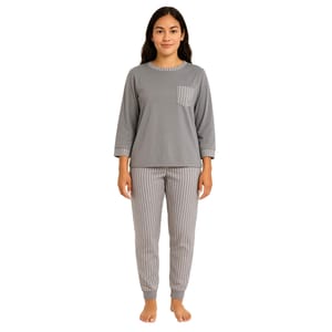 A woman is wearing a grey pajama set with a long-sleeve top featuring a pocket and striped collar and cuffs, paired with matching striped pants.