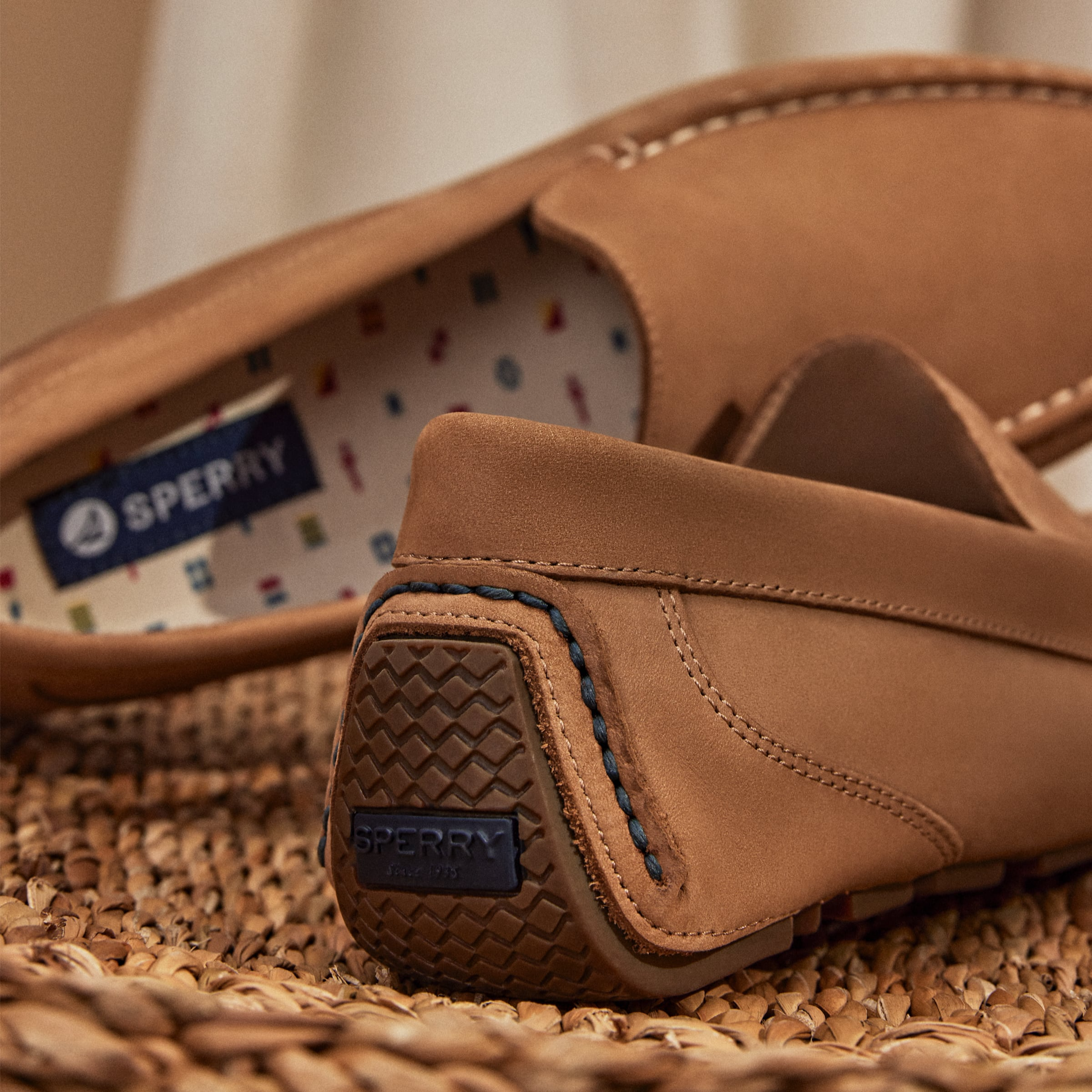 A pair of brown Sperry loafers with patterned insoles displayed on a woven surface.