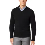 A man is wearing a black V-neck sweater over a blue and white checkered shirt, paired with gray pants.