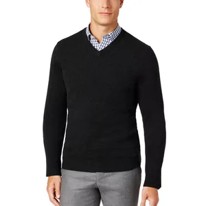 A man is wearing a black V-neck sweater over a blue and white checkered shirt, paired with gray pants.