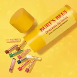 Burt's Bees lip balms in various flavors, including beeswax with vitamin E and peppermint, vanilla maple, mint cocoa, and sugar cookie, are displayed against a yellow background.