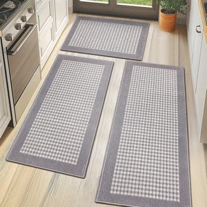 Three rectangular kitchen rugs with a checkered pattern and gray borders are arranged on a light-colored floor.