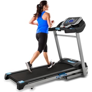 A woman is running on an XTERRA Fitness folding treadmill, which features a digital display with control buttons, a safety rail, and a cushioned running surface.