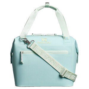 Light teal cooler bag with a zippered front pocket, handles, and an adjustable shoulder strap. Features the Stanley logo and designed for transport and insulation.