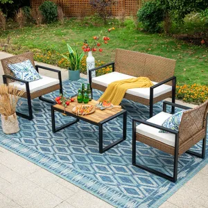 Outdoor patio set with two armchairs, a loveseat, and a wooden coffee table on a blue patterned rug. Includes white cushions, decorative pillows, a yellow throw, and is accessorized with a plant, vase of flowers, drinks, and a cheese platter.