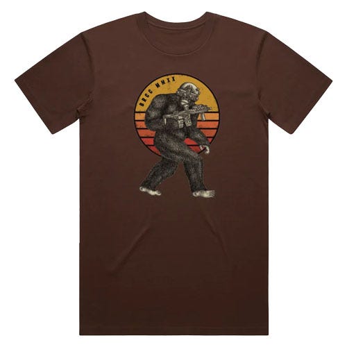 A brown t-shirt featuring a graphic of a Bigfoot figure holding a firearm, set against a retro-style circular background with yellow and red stripes. The text above the image reads \“HICC WAXX\“.