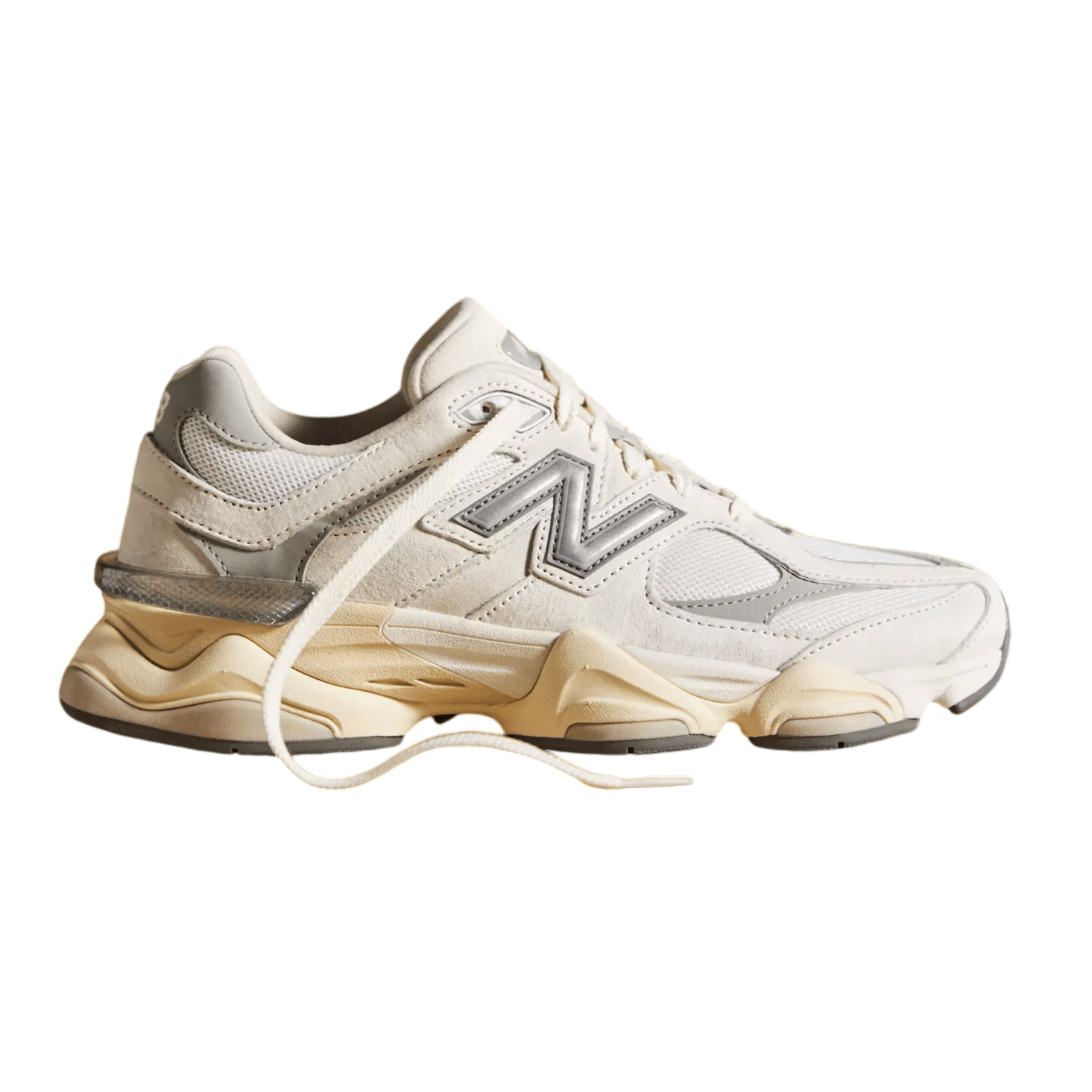 A cream-colored New Balance sneaker with a silver \“N\“ logo and beige sole, featuring a chunky design and a mesh and suede upper.