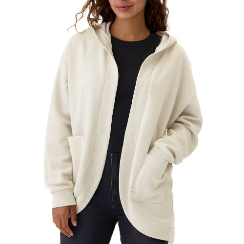 A woman wearing a plain cream-colored zip-up hoodie with pockets and a dark top underneath.