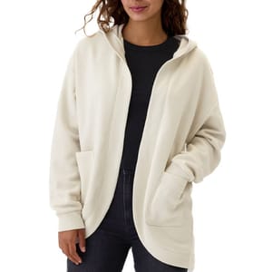 A woman wearing a plain cream-colored zip-up hoodie with pockets and a dark top underneath.