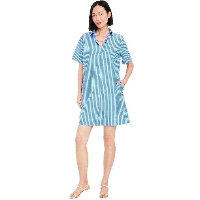 A woman is wearing a blue and white striped button-up shirt dress with short sleeves, accessorized with a necklace and white sandals.