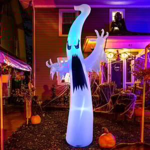 Inflatable Halloween ghost decoration with menacing expression stands in a yard, surrounded by pumpkins and cobwebs, illuminated with colorful lighting.