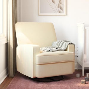 A cream-colored glider chair with a simple, modern design is placed on a pink rug, next to a crib. A gray striped blanket is draped over the armrest, and there are wooden blocks nearby on the floor.