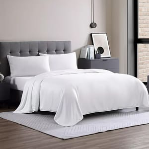 White queen-sized comforter on a neatly made bed with a gray tufted headboard; part of a modern, minimalistic bedroom setup featuring a gray nightstand, decorative books, and a framed artwork, all on a soft, light-colored rug.