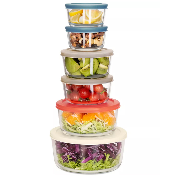 A 12-piece glass bowl set featuring six stackable round bowls with multi-colored plastic lids. These bowls contain an assortment of fruits, vegetables, and salads, demonstrating their use for food storage or serving.
