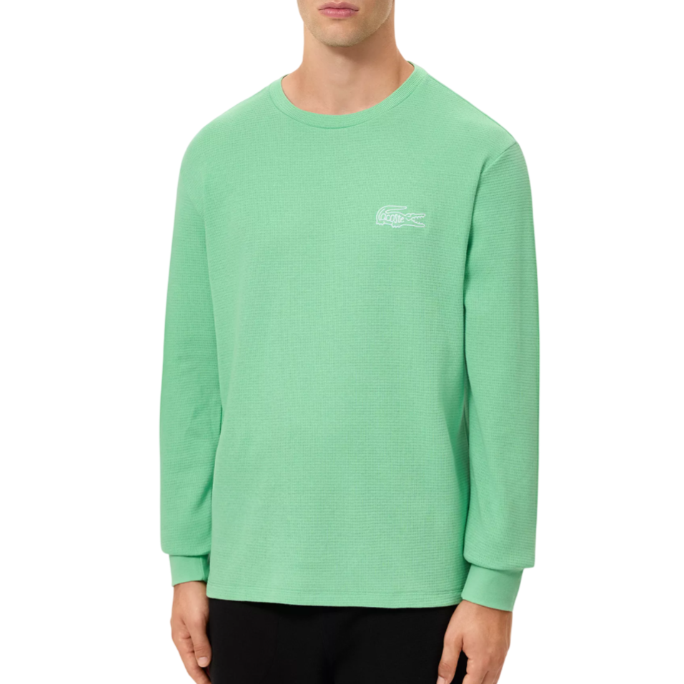 Mint green long-sleeve crew-neck shirt with a subtle waffle texture and a white embroidered logo on the chest, paired with black pants.