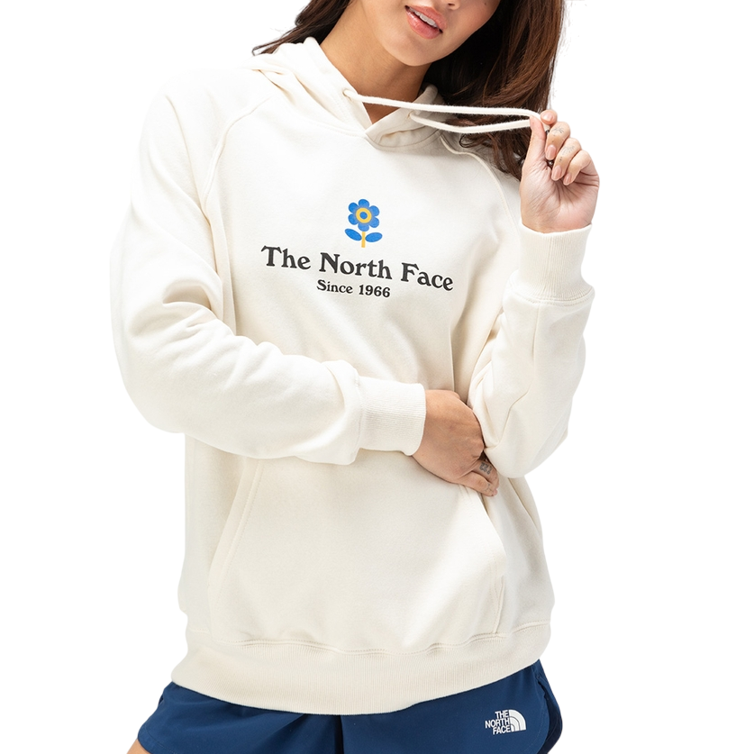 A person is wearing a white hoodie featuring The North Face logo and \“Since 1966\“ text, along with blue shorts also branded with The North Face logo.