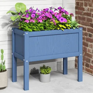 A blue wooden raised planter box filled with green and purple flowers is against a brick and white siding backdrop. Nearby, a potted cactus and a small plant in a gray pot add decorative touches.