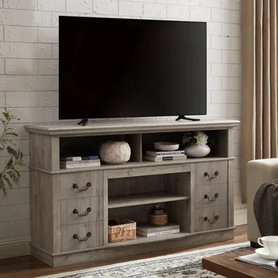 A wooden TV stand with drawers and shelves holds a flat-screen TV. Decorations, books, and a woven basket are arranged on the shelves, complemented by a cream curtain and a patterned rug.