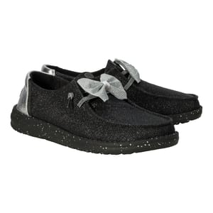 Hey Dude Wendy Sparkle Bow shoes feature a black, glittery finish with a large silver bow on the top. They have a speckled black sole and metallic silver detailing at the heel, offering a stylish and casual look.