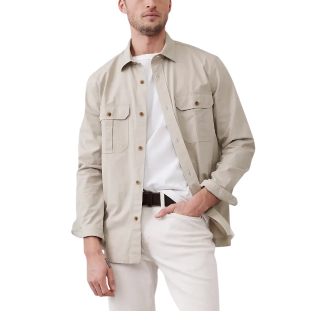 A beige overshirt featuring a button-up front, two chest pockets with flaps, and long sleeves. It is worn with a white t-shirt, light-colored pants, and a black belt.