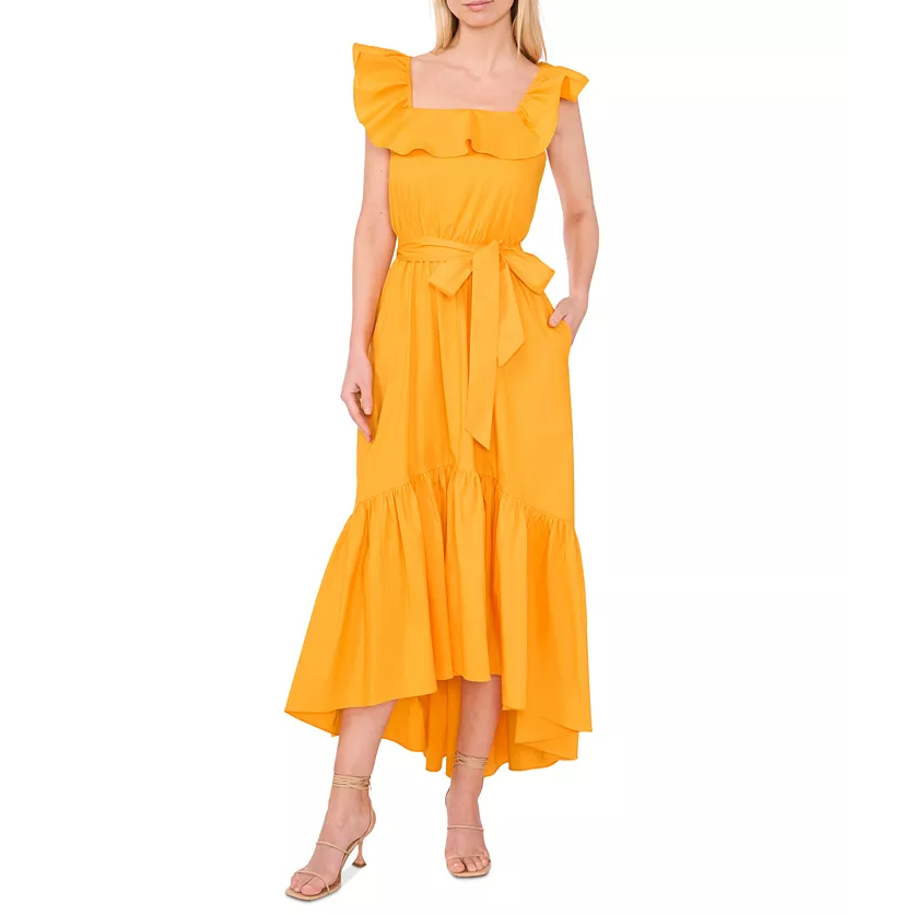 A woman is dressed in a sleeveless, ruffled, high-low hem, bright yellow dress with a tied waist, complemented by strappy beige heels.