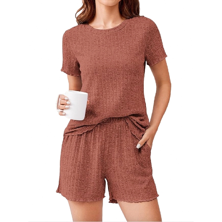 A woman is wearing a two-piece loungewear set in a textured, dusty rose color, featuring a short-sleeved top and matching shorts. She's holding a white mug in one hand, and the other hand is casually placed in her shorts pocket.