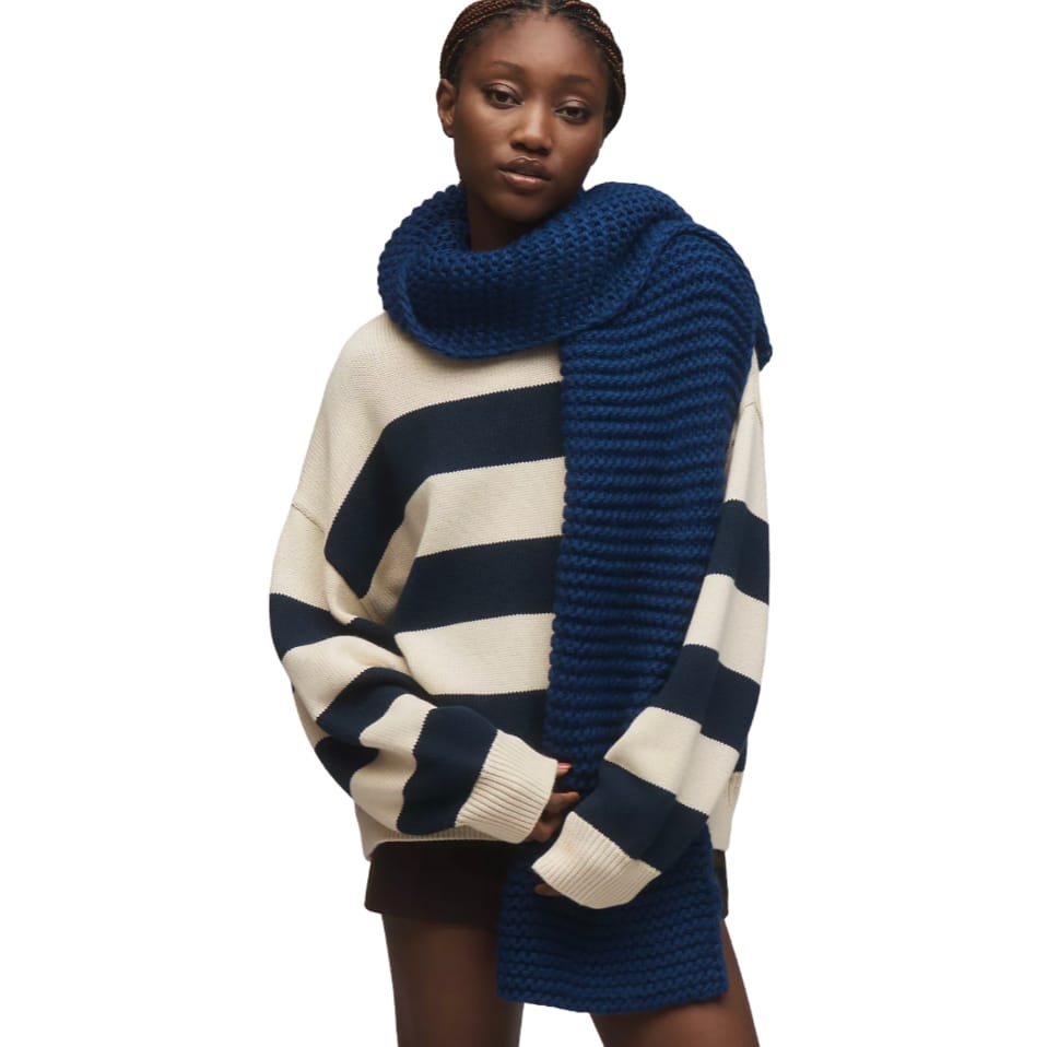 A thick, ribbed knit scarf in a deep blue color, measuring 72 inches long, draped over a person wearing a cream and navy striped sweater.