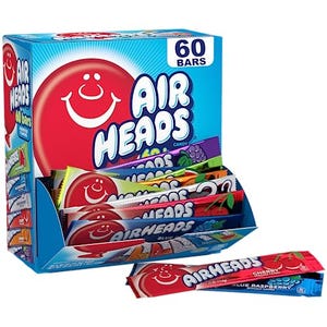 A 60-count box of full-size Airheads candy bars opened to display a variety of flavors. A single Airheads bar in Blue Raspberry flavor lies in front of the box.