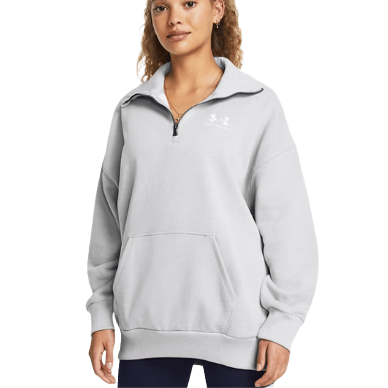A woman wears a light gray Under Armour Women's Oversized Jacket featuring a quarter-zip front, a high collar, a kangaroo pocket, and ribbed cuffs and hem.