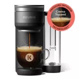 A Keurig coffee maker featuring Pressure Infusion Technology for crema-topped coffee, shown brewing into a glass mug.