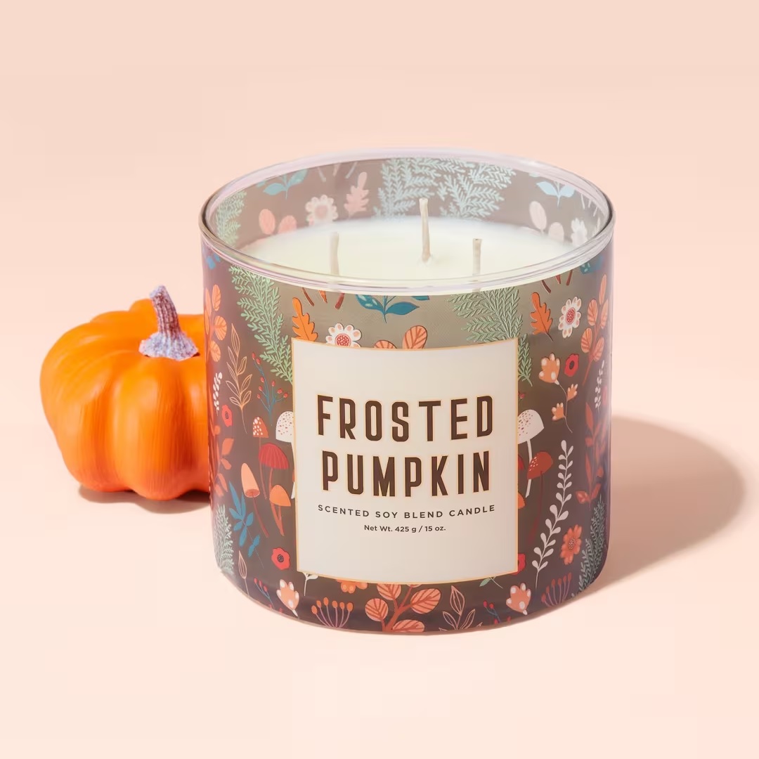 A frosted pumpkin scented soy blend candle with three wicks, next to a small decorative pumpkin.