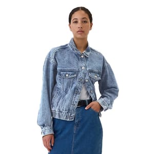 A light blue denim bomber jacket with a stonewashed finish, featuring a button-up front, two chest pockets with button flaps, and an elasticized waistband. It is paired with a high-waisted blue denim skirt and a white shirt.