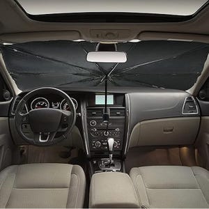 A car sunshade shaped like an umbrella is deployed behind the windshield, blocking sunlight from entering the vehicle's interior.
