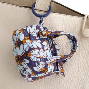 A small, floral-patterned fabric bag is attached to a larger cream-colored leather bag using a blue ring clip.