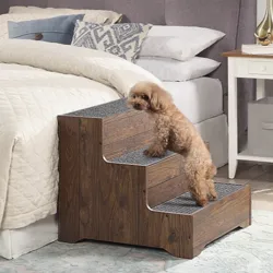 A small dog climbs wooden pet stairs beside a bed in a cozy bedroom, featuring a white nightstand and a decorative lamp.