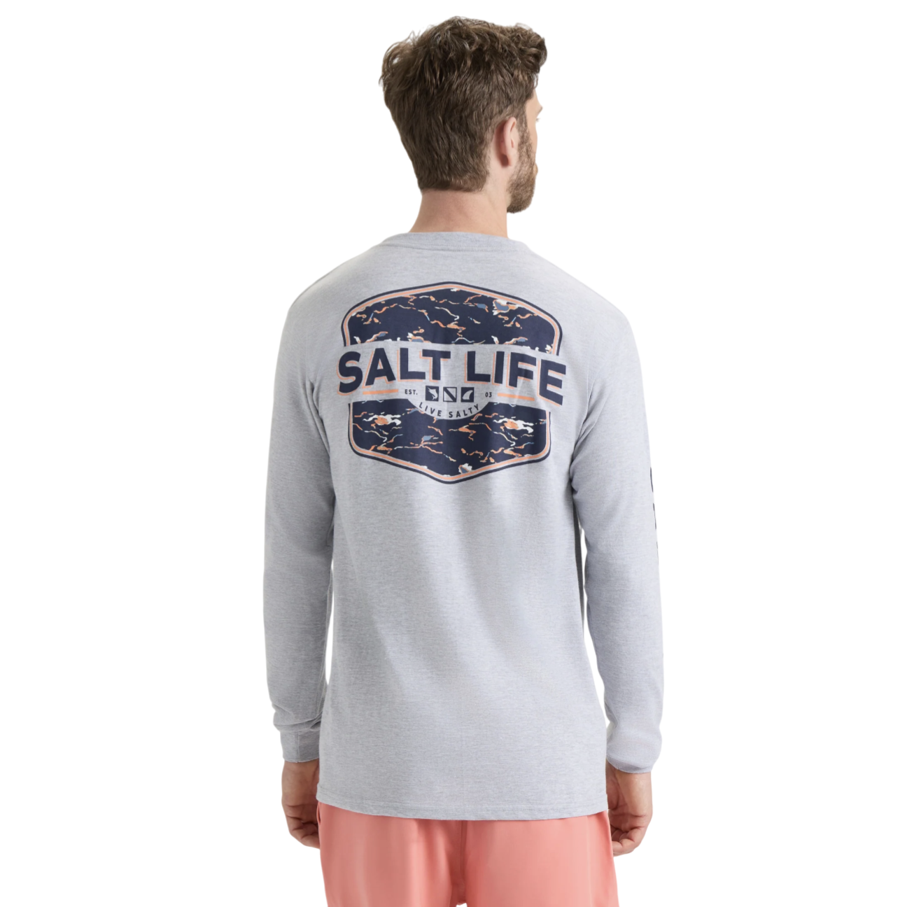 A man is wearing a light gray long-sleeve shirt with a large \“Salt Life\“ logo and graphic on the back, paired with coral-colored shorts.