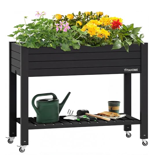 A raised garden bed on wheels with a shelf below, filled with various flowering plants. Gardening tools, a watering can, and plant pots are placed on the lower shelf.