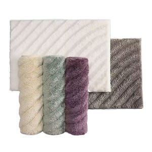 Vera Wang Luxury Bath Rug features a plush, textured design in soft colors: cream, mint, purple, gray, and white. The set includes one large rectangular rug and three rolled smaller rugs, each with a subtle diagonal stripe pattern.