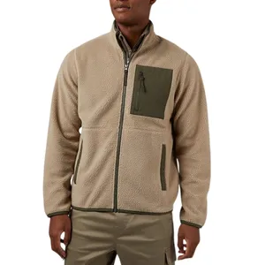 A man is wearing a tan fleece zip-up jacket with a dark green chest pocket and matching green accents. He's paired it with khaki pants.