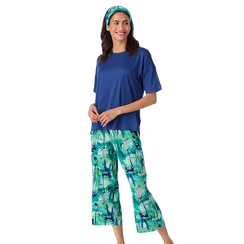 A woman is wearing a blue short-sleeve top with green, tropical-patterned pajama pants, and a matching headband.