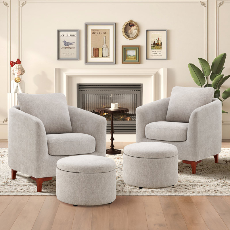 A living room setup features two grey swivel chairs with wood legs, matching ottomans, a small round side table, and wall decor, all set against a white fireplace backdrop.