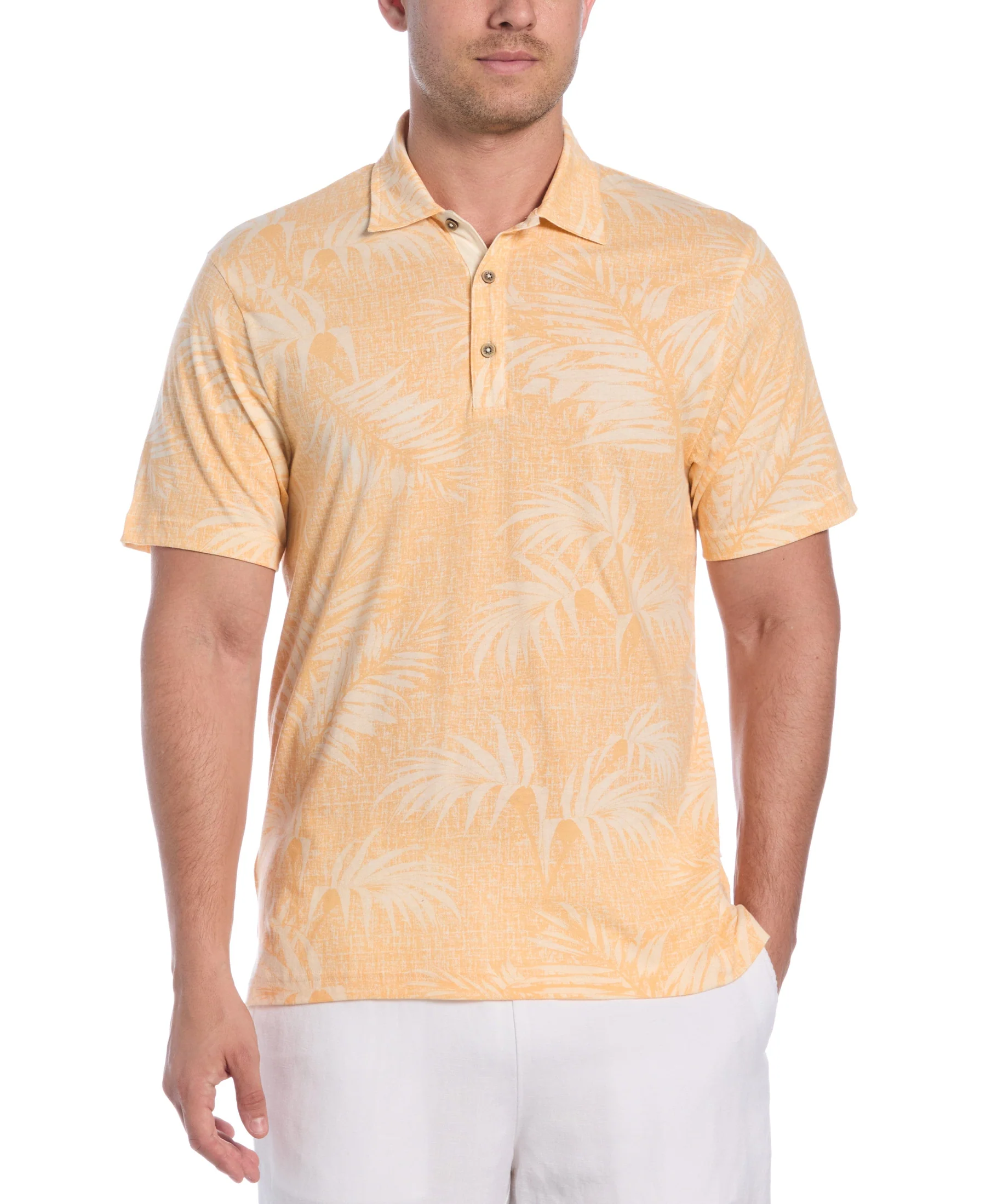 A man is wearing a light orange polo shirt with a subtle palm leaf pattern, paired with white pants.